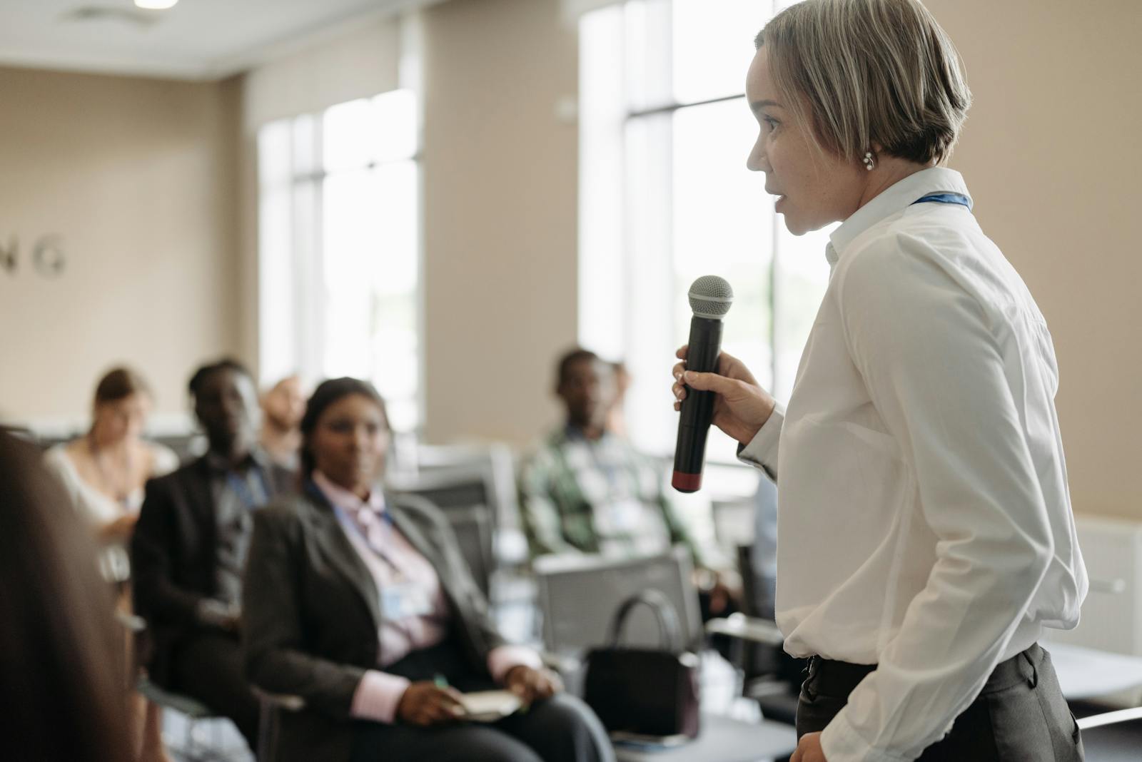 Side view of a woman holding a microphone while addressing an audience at a conference.